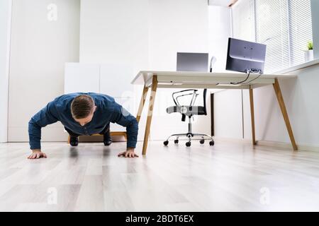 Businessman Doing Push Up On Hardwood Floor In Office Stock Photo