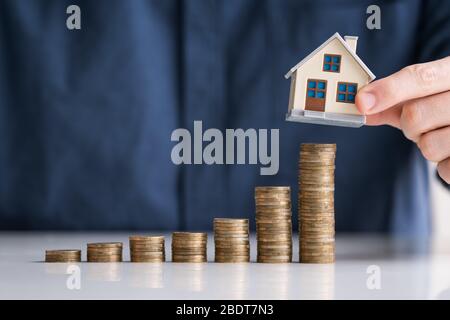 Close-up Of Businessman Hand Arranging House Model On Stacked Coins At Desk Stock Photo