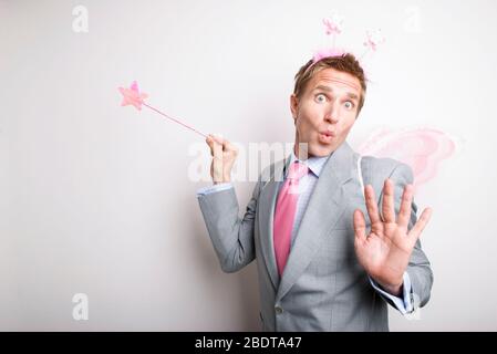 Fairy businessman waving a pink glittery star magic wand granting a wish with a funny expression on his face Stock Photo
