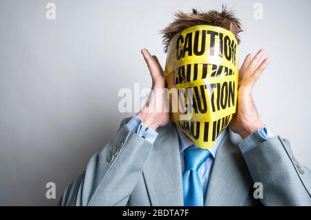 Unrecognizable businessman pressing his hands to his head, wrapped in yellow and black caution tape Stock Photo