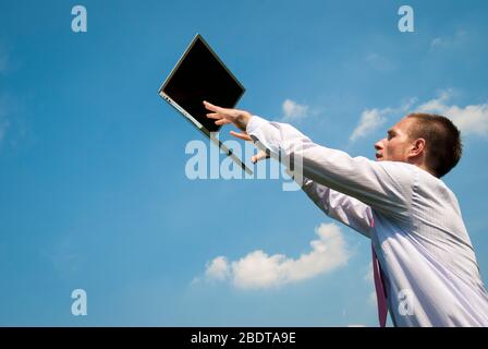Office worker reaching up to type on a mobile laptop floating outdoors in sunny blue sky Stock Photo