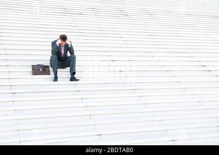 Distant businessman sitting outdoors on a large, lonely white staircase Stock Photo