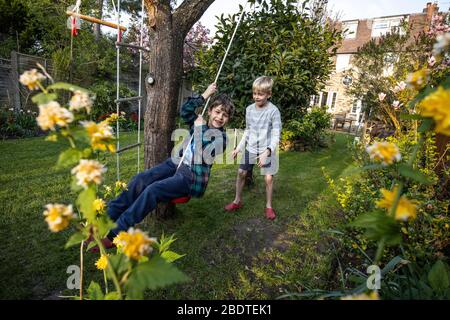 Two young brothers aged 6 and 9 playing on a rope ladder and rope swing in their back garden, London, England, United Kingdom Stock Photo