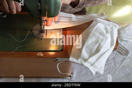 Woman hands using the sewing machine to sew face medical mask at home. Handmade protective mask against coronavirus. Stock Photo