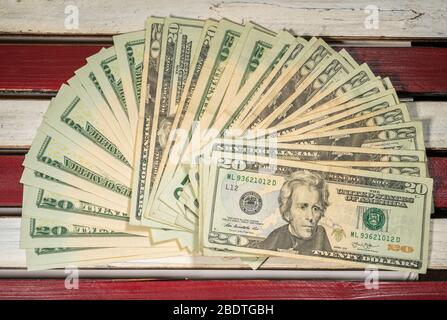 Thousands of US dollars laid out in a fan shape with 20 dollar bills on wooden USA flag Stock Photo