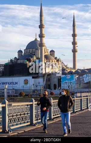 April 7, 2020: Masked citizens walking on Galata Bridge, which is normally quite crowded, with New Mosque in background, near Eminonu district, Istanbul, TURKEY, on April 3, 2020. Turkish officials have repeatedly urged citizens to stay home and respect social distancing rules. Turkey continues to implement measures to contain the spread of the virus and to avoid a full lockdown, issuing stay-at-home orders for all persons over 60 and under 20 years of age, closing road borders of 31 cities, closing bars, cafes and restaurants and limiting public gatherings.Turkey on 7th of April confirmed 3, Stock Photo
