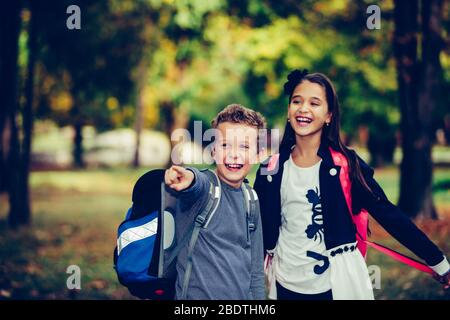 Back to school. Close up two happy friends with backpacks laughing and having fun in the park. Boy and girl holding books on the first school day.  Ki Stock Photo