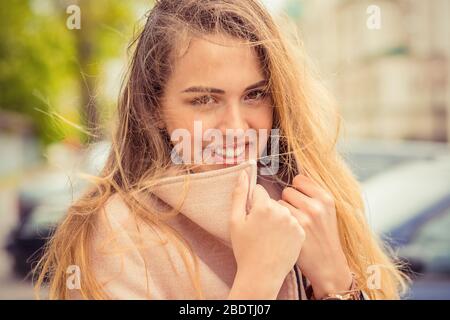 Windy. Woman happy hair on face. Closeup portrait beautiful smiling toothy sunshine girl student having cold holding collar neckband looking at you ca Stock Photo