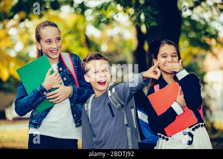Back to school. Close up three happy friends with backpacks laughing and having fun in the park. Boy and girl holding books on the first school day. K Stock Photo