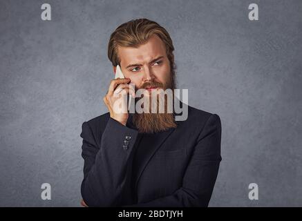 Cool young man with beard walking and talking with mobile phone isolated grey background wall Stock Photo