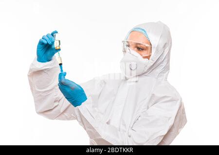 Female doctor in a protective white suit with a syringe in his hands and blue rubber gloves stands in different poses Stock Photo