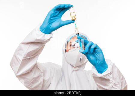 Female doctor in a protective white suit with a syringe in his hands and blue rubber gloves stands in different poses Stock Photo