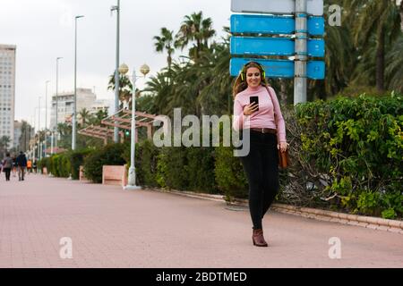Young woman walks on the street listening music with her headphones Stock Photo