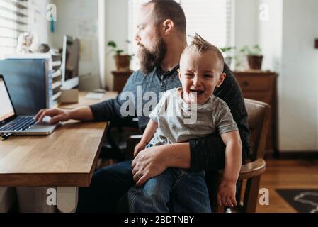 Father trying to work from home with toddler screaming in his lap Stock Photo