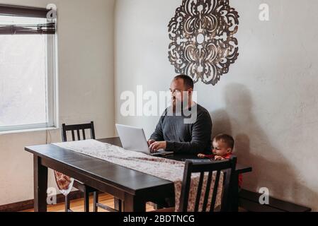 Wide view of father trying to work from home with toddler standing Stock Photo