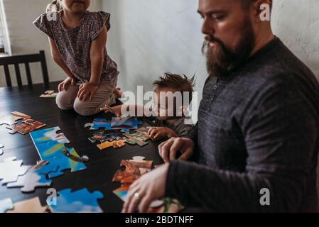 Family with young children completing puzzle at home during isolation Stock Photo