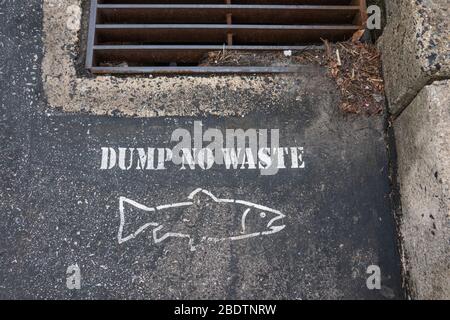 Dump No Waste and the outline of a fish stenciled on the blacktop of a parking lot near a storm drain Stock Photo