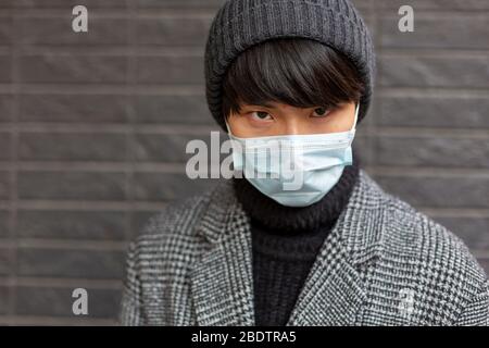 Young Chinese guy in medical mask and hat looks up angry. Pandemic disease Stock Photo