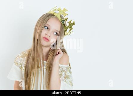Mini Miss. Young bored girl wearing a crown and a white dress on Holiday looking side wards isolated white background Stock Photo