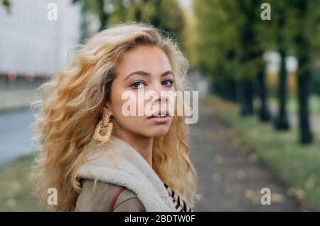 Young blond girl walking in public park in fall and looking to camera Stock Photo