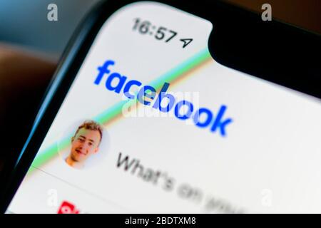 Facebook App on iPhone with people using tablet background closeup male ...