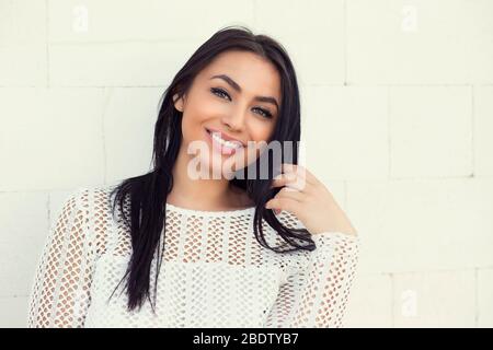 Closeup portrait of confident smiling happy pretty young woman in white shirt, isolated background white wall background. Positive human emotion facia Stock Photo