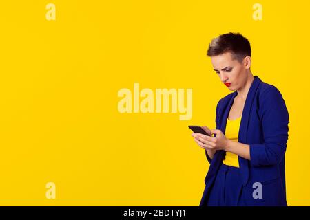 Portrait young angry woman unhappy, annoyed by something, someone on her cell phone texting, receiving bad sms text message news isolated yellow wall Stock Photo