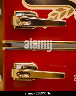 Symmetrical Close Up of Two Chrome Fridge Door Handles on Old Antique Red Refrigerator With Gold Leaf Decor Stock Photo