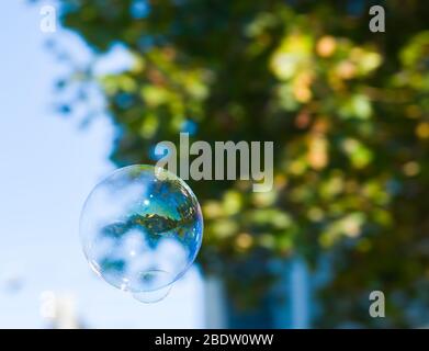 Image of a House Seen Inside a Blown Bubble Floating in the Air with Fall Leaves of a tree behind  symbolising dream house or real estate industry Stock Photo