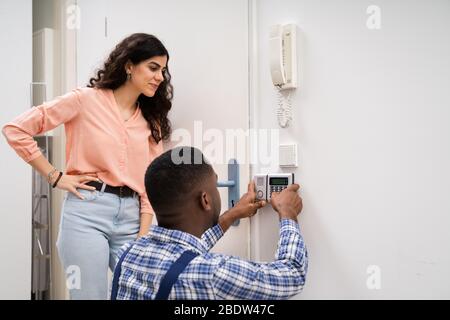Close-up Of Handyman Installing Security System Near Door Wall While Woman Using Remote Stock Photo