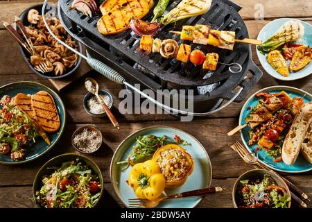 Various vegetables on a grill and healthy, gourmet dishes on a rustic timber table. Stock Photo