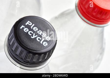 Plastic bottles and black and red bottle caps with please recycle message against a white background. Concept of plastic pollution. Stock Photo