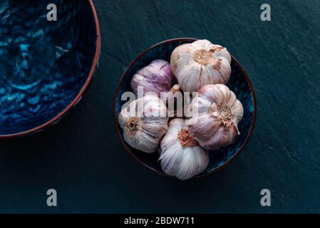 Garlic. Fresh garlic bulbs in vintage bowl over dark stone background. Top view on dark stone table. Stock Photo