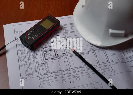 Laser meter, white hardhat and drawings at engineer workplace. Stock Photo