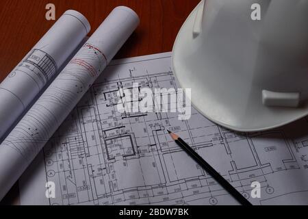 White hardhat and drawings at engineer workplace. Stock Photo