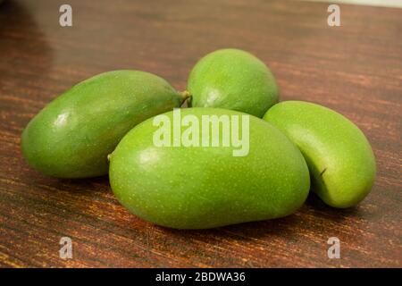 Organic Young Green Mangoes Branch Macro isolated on Wooden Table sour fruits. Stock Photo