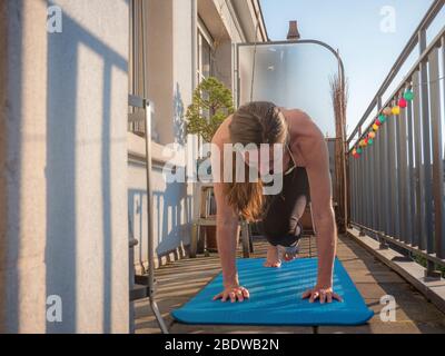 A woman practices yoga on the balcony of her apartment during the Covid-19 lock down in Geneva, Switzerland. The sun shines on the balcony as she maxi Stock Photo