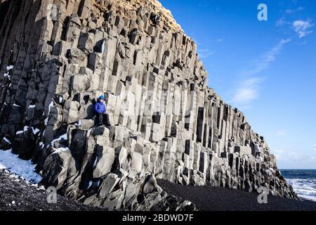 A woman sitting on basalt columns at Reynisfjara black sand beach in winter near Vík í Mýrdal, southern Iceland Stock Photo
