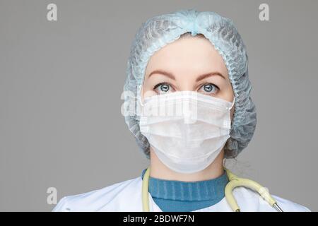 Beautiful woman doctor in white medical clothes, mask, phonendoscope and medical hat, picture isolated on blue background Stock Photo