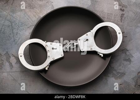Handcuffs in a black plate, top view. Food Poison Punishment Concept Stock Photo