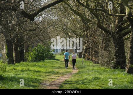 London, UK - 09 April 2020: A couple walk by a woody path on Wanstead Park as the weather warmed up ahead of the Easter weekend.    The government has advised the public to stay at home in the UK due to the Covid-19 pandemic but for essential trips for basics and exercise. Photos: David Mbiyu Stock Photo
