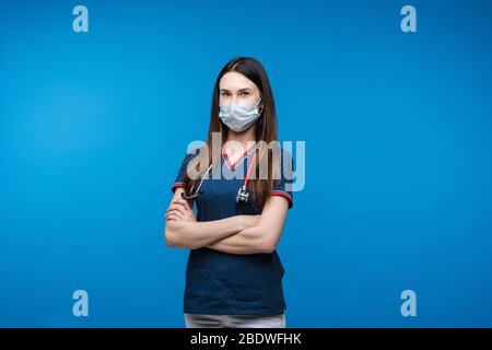 Lovely woman doctor in white medical clothes, mask, phonendoscope confidently stands with hands on her chest, picture isolated on blue background Stock Photo
