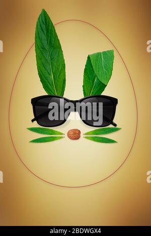 Easter eggs with Bunny rabbit face inside, made of natural green leaves with sunglasses on bright background. Easter minimal concept. Flat lay Stock Photo