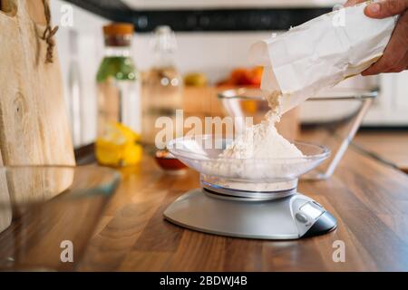 Woman adding flour to an electronic weight to make pizza dough in her home kitchen Stock Photo