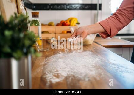 Woman putting flour on wooden kitchen counter to knead pizza dough Stock Photo