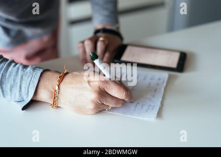 Woman making a shopping list in the kitchen. Stock Photo