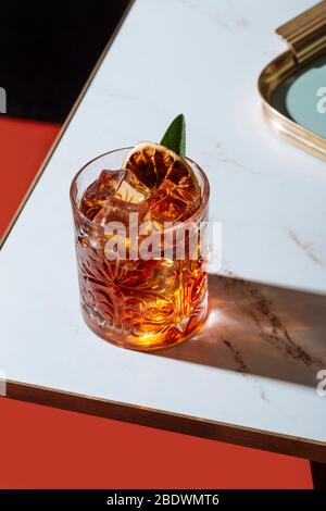 Gin tonic and Negroni cocktail, with charred orange, lemon slice and blooming rosemary, on a small table. Vintage aesthetic with star filter Stock Photo