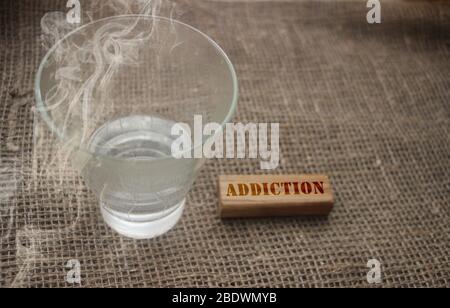 Almost empty glass with cigarette smoke and addiction word on wooden block. Alcoholism and smoking addicted concept Stock Photo
