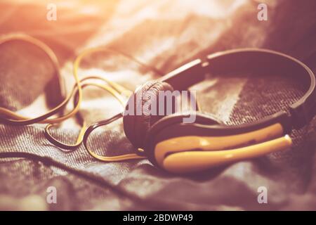 Yellow headphones with a tangled wire lie on a soft wool plaid blanket, illuminated by the midday sun. Stock Photo