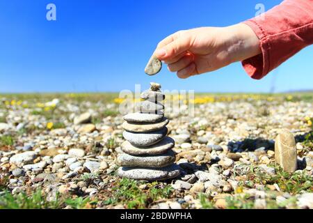 Kid's hand fixing rock on the top of stone stack Stock Photo